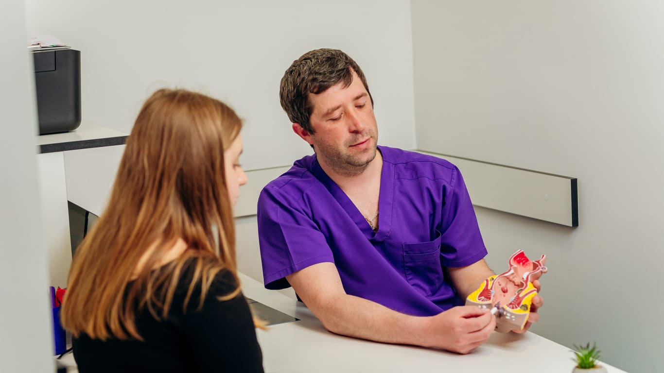 Ein Arzt zeigt einer Patientin ein Modell der Analregion