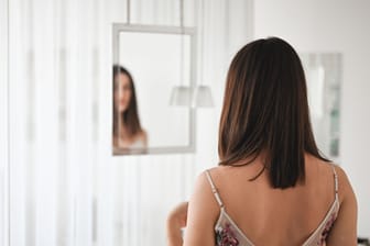 Rückansicht einer Frau, die sich im Spiegel betrachtet