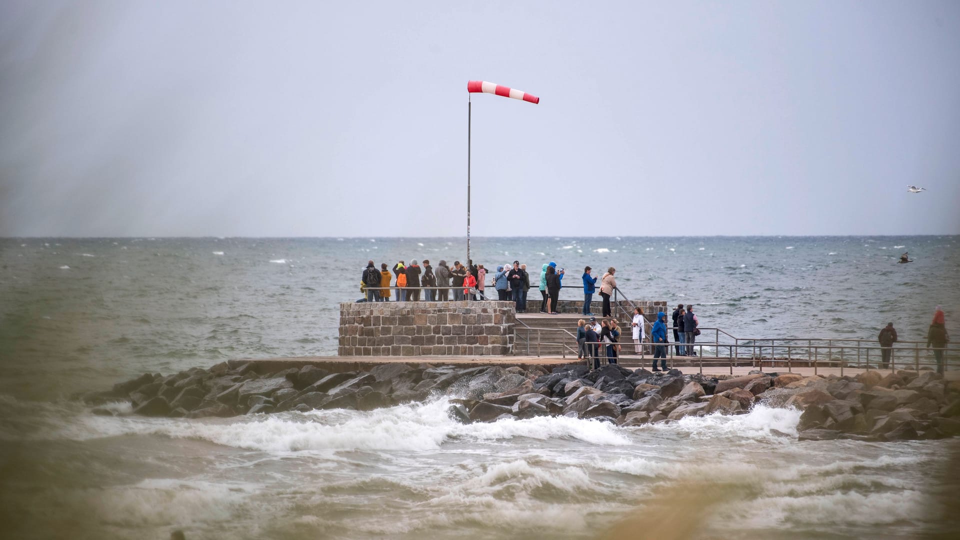 Urlauber stehen im Wind auf der Mole im Ostseebad Warnemünde.