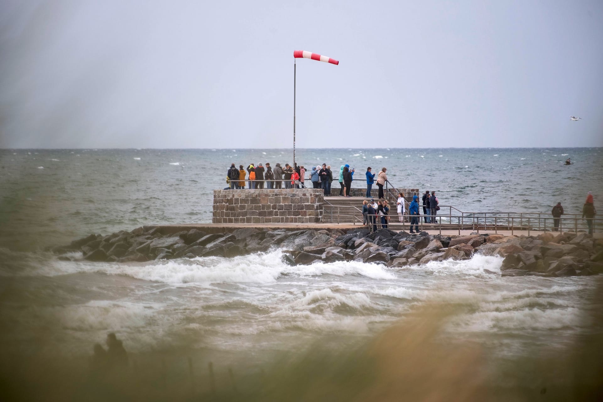 Urlauber stehen im Wind auf der Mole im Ostseebad Warnemünde.