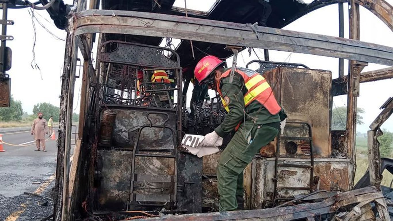 Rettungskräfte untersuchen den verbrannten Bus an der Unfallstelle auf einer Autobahn.