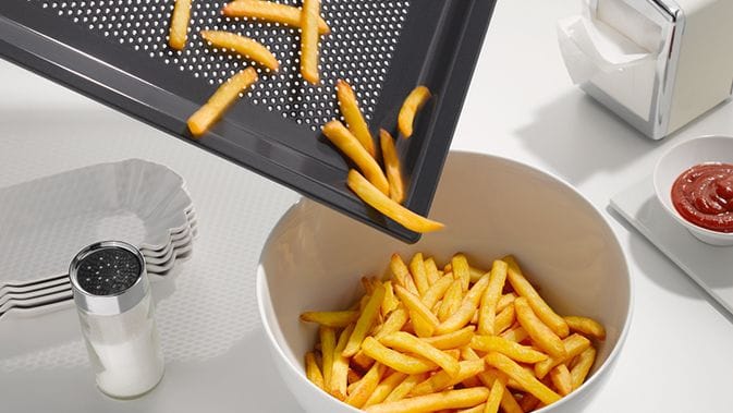 Pommes Frites werden von einem gelochten Air-Fryer-Brech in eine Schüssel geschüttet: Miele