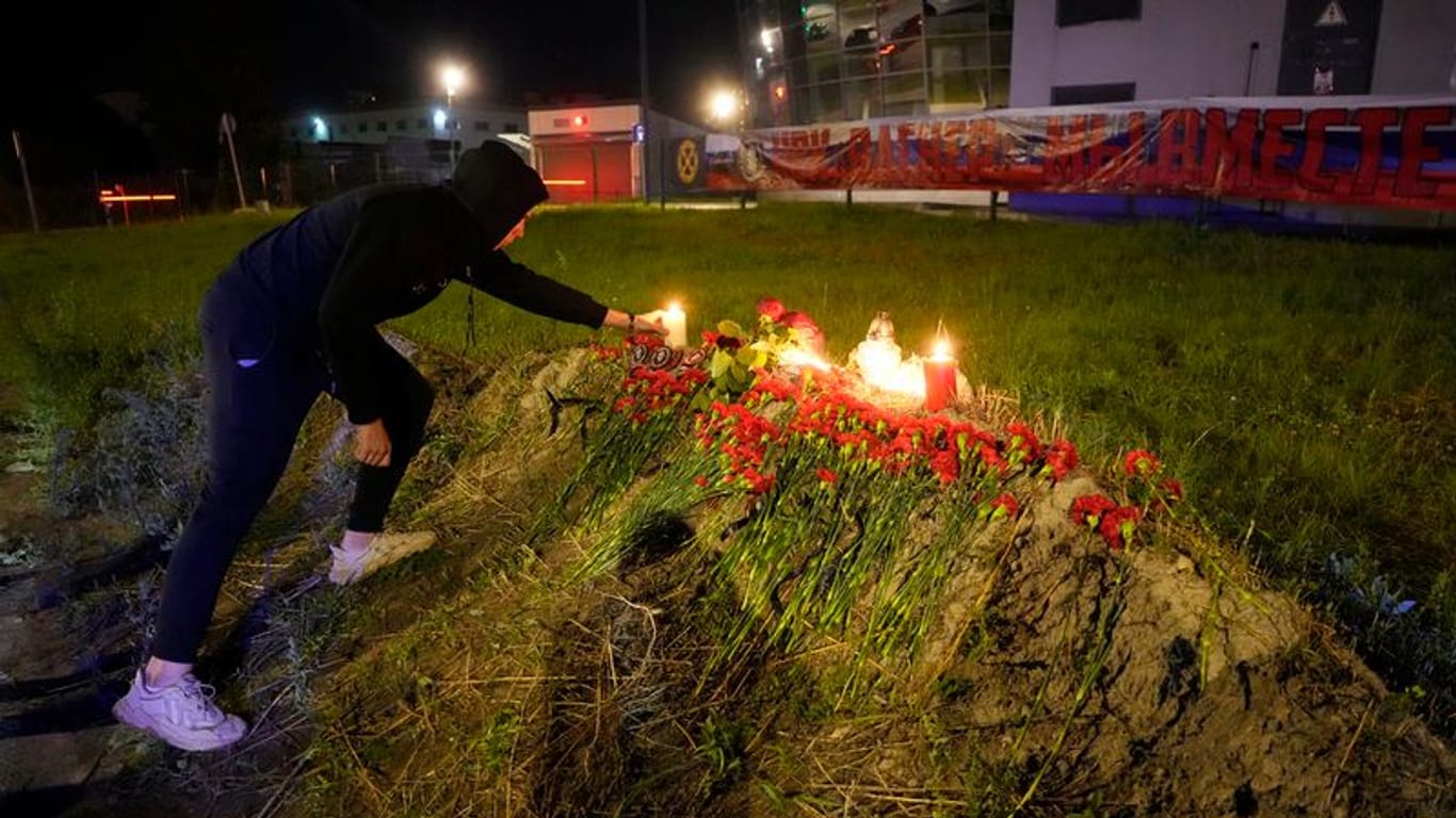 Ein Mann zündet eine Kerze an einer informellen Gedenkstätte neben dem ehemaligen "PMC-Wagner-Zentrum" in St. Petersburg an. Im Hintergrund hängt ein Banner: "PMC Wagner, wir sind zusammen".