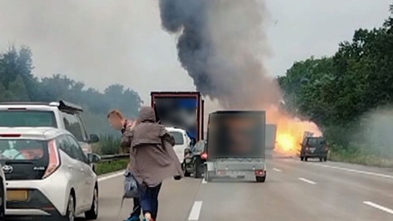 Autofahrer verlassen ihre Fahrzeuge, während im Hintergrund ein Lkw in Flammen steht.
