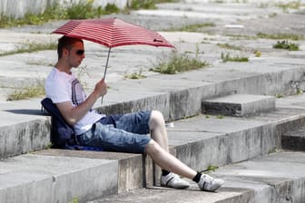 Ein Mann versucht sich mit einem Sonnenschirm vor der Hitze zu schützen (Symbolbild): Wetterdienst spricht Hitzewarnung für Nürnberg aus.