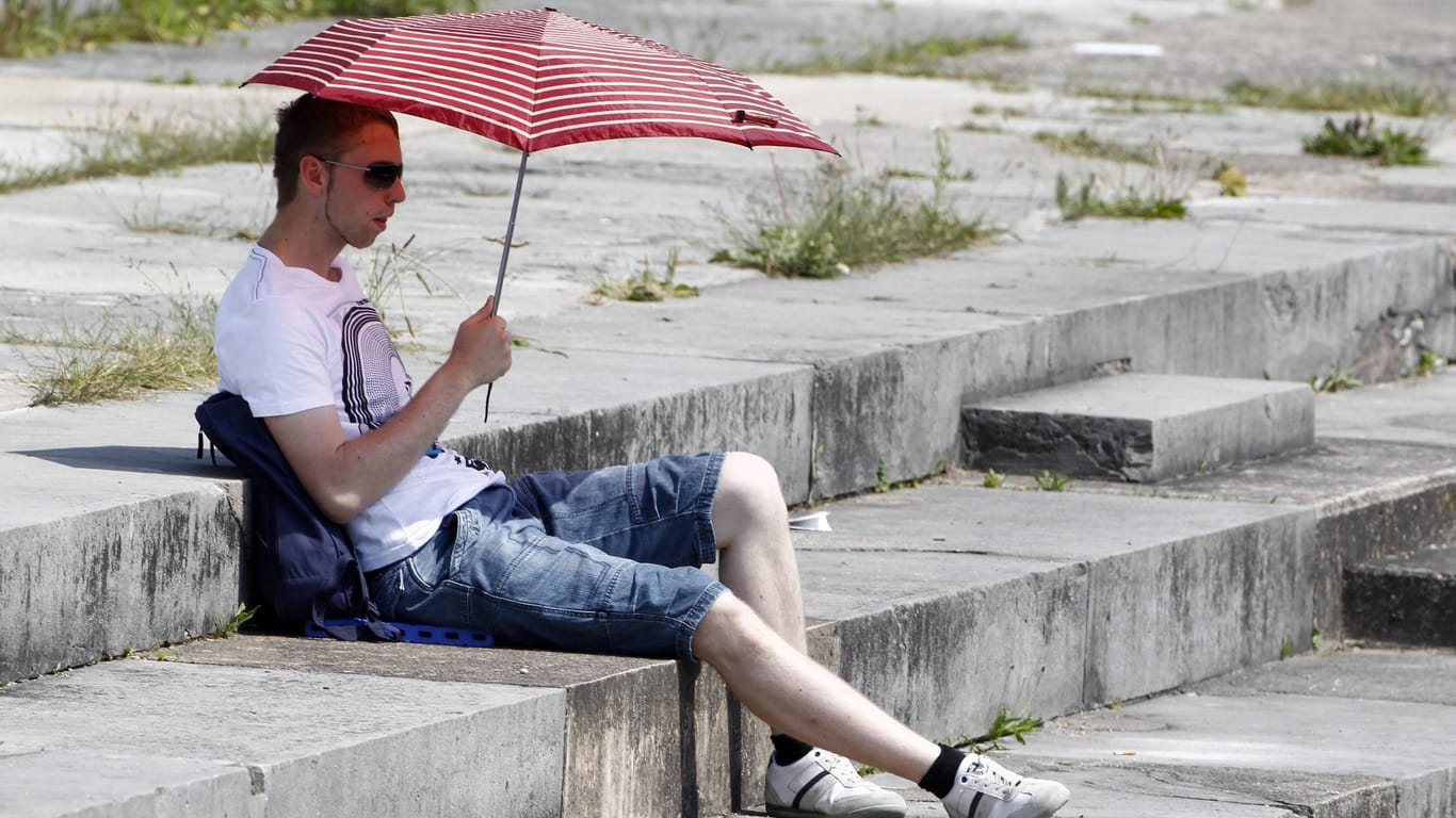 Ein Mann versucht sich mit einem Sonnenschirm vor der Hitze zu schützen (Symbolbild): Wetterdienst spricht Hitzewarnung für Nürnberg aus.