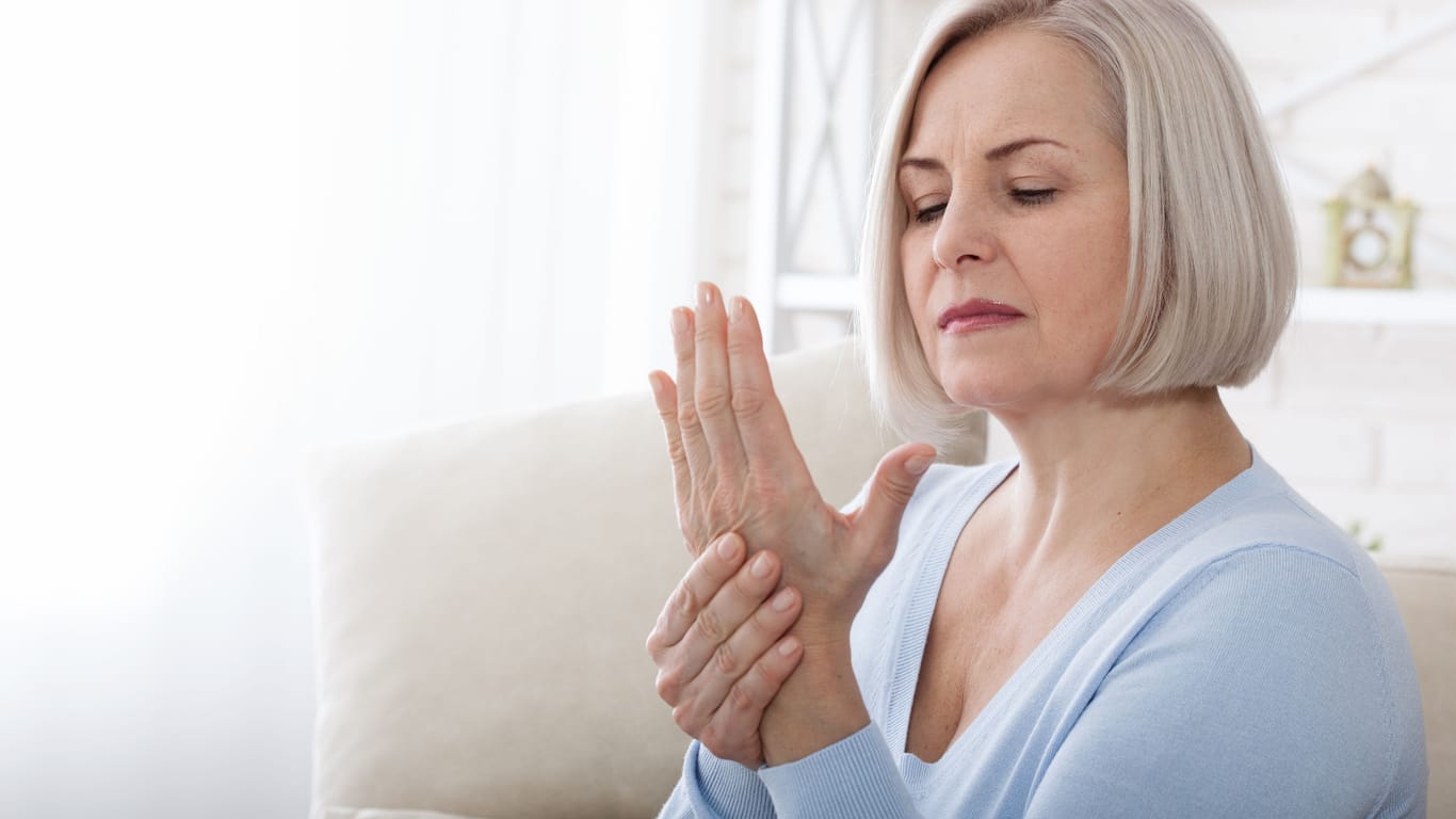Eine ältere Frau betrachtet ihre linke Hand: Bei Frauen zeigen sich erste Anzeichen einer Heberden-Arthrose oft in den Wechseljahren. Nicht immer ist eine Therapie nötig.