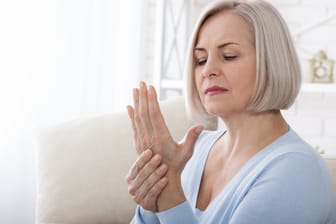 Eine ältere Frau betrachtet ihre linke Hand: Bei Frauen zeigen sich erste Anzeichen einer Heberden-Arthrose oft in den Wechseljahren. Nicht immer ist eine Therapie nötig.