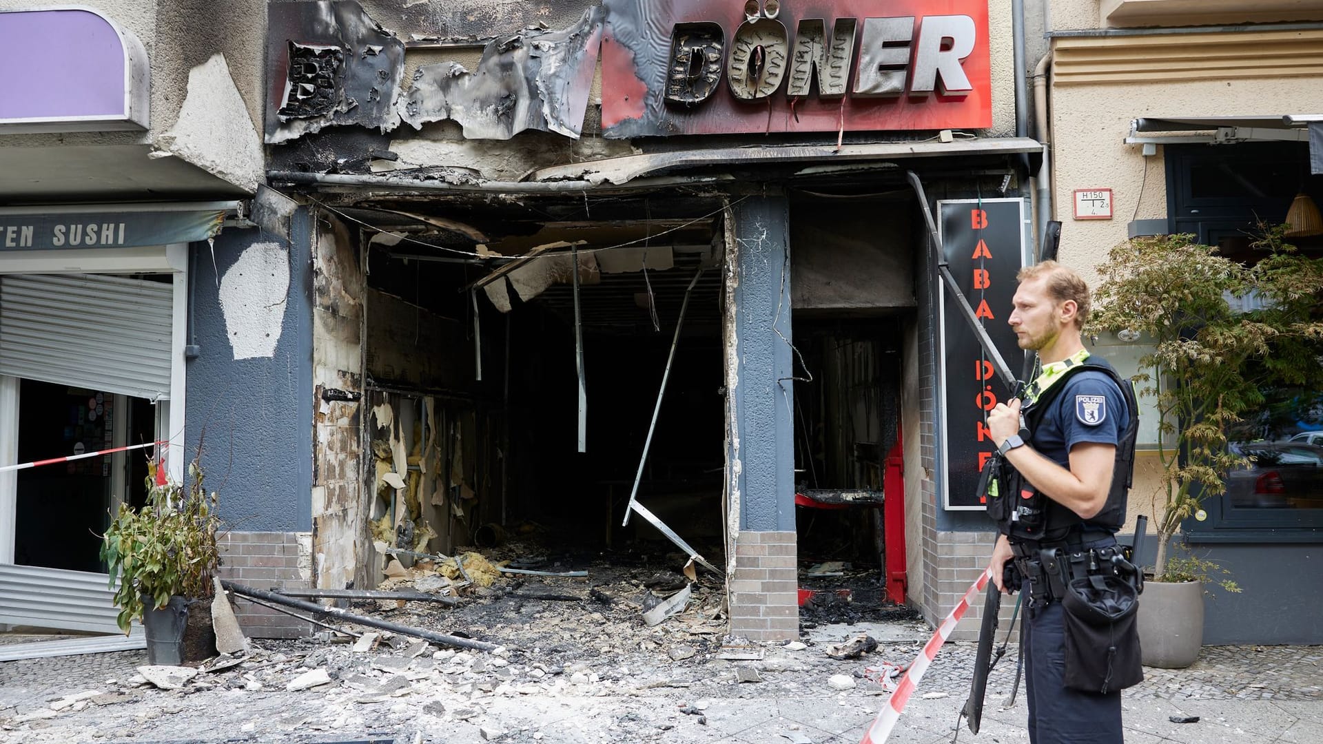 Ein Polizist steht vor dem ausgebrannten Dönerimbiss in der Uhlandstraße: Das Brandkommissariat ermittelt nun der Polizei zufolge in alle Richtungen.