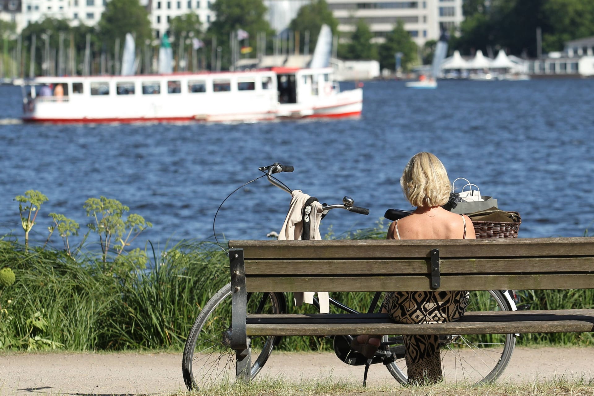 Eine Frau sitzt auf einer Bank und schaut auf die Außenalster (Symbolfoto): Zum Start in die neue Woche wartet sommerliches Wetter.