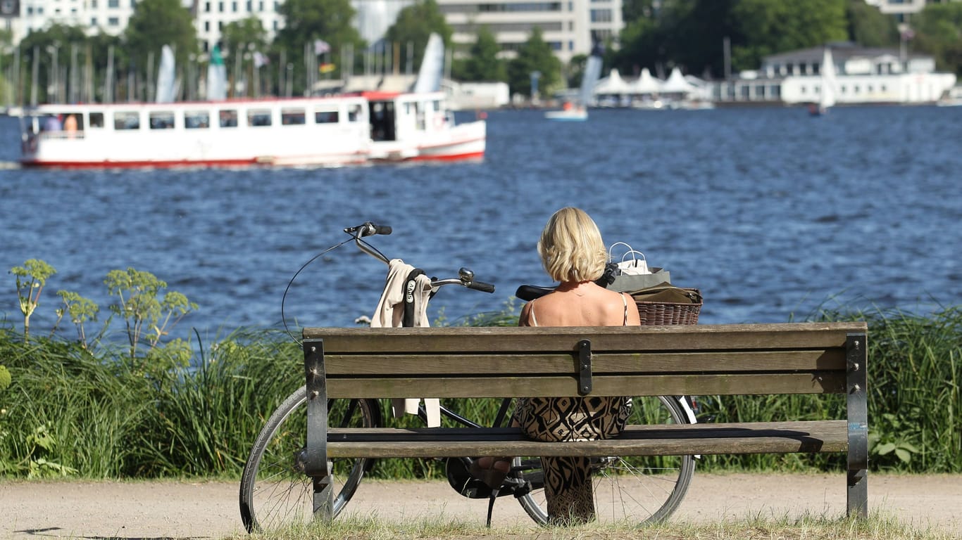 Eine Frau sitzt auf einer Bank und schaut auf die Außenalster (Symbolfoto): Zum Start in die neue Woche wartet sommerliches Wetter.