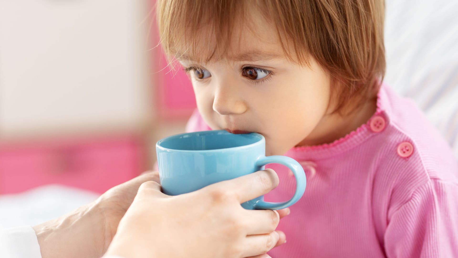 Jemand hält einem Kind im Bett eine Tasse an den Mund