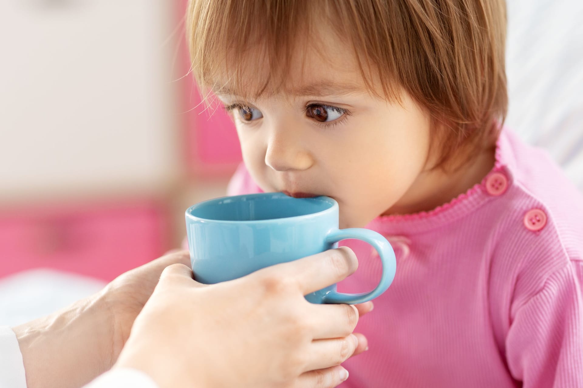 Jemand hält einem Kind im Bett eine Tasse an den Mund