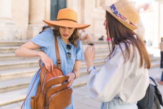 Eine Touristin blickt erschrocken in ihren Rucksack: Taschendiebe sind vor allem an beliebten Urlaubsorten aktiv.