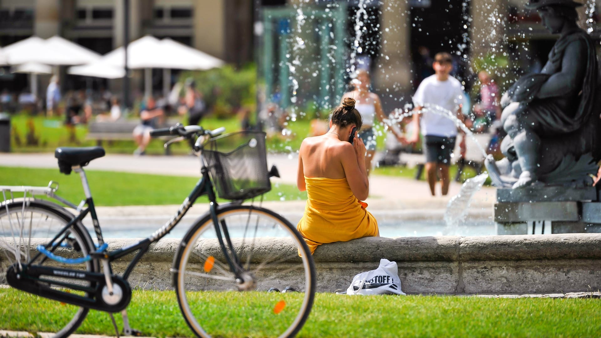 Eine Frau sitzt bei Hitze am Stuttgarter Schlossplatz (Archiv): Von Sommerwetter ist in Baden-Württemberg derzeit keine Spur.