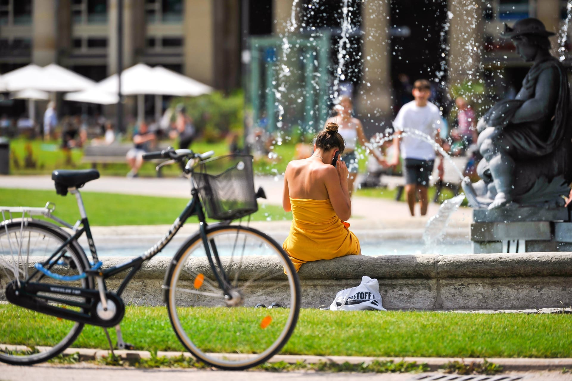 Eine Frau sitzt bei Hitze am Stuttgarter Schlossplatz (Archiv): Von Sommerwetter ist in Baden-Württemberg derzeit keine Spur.