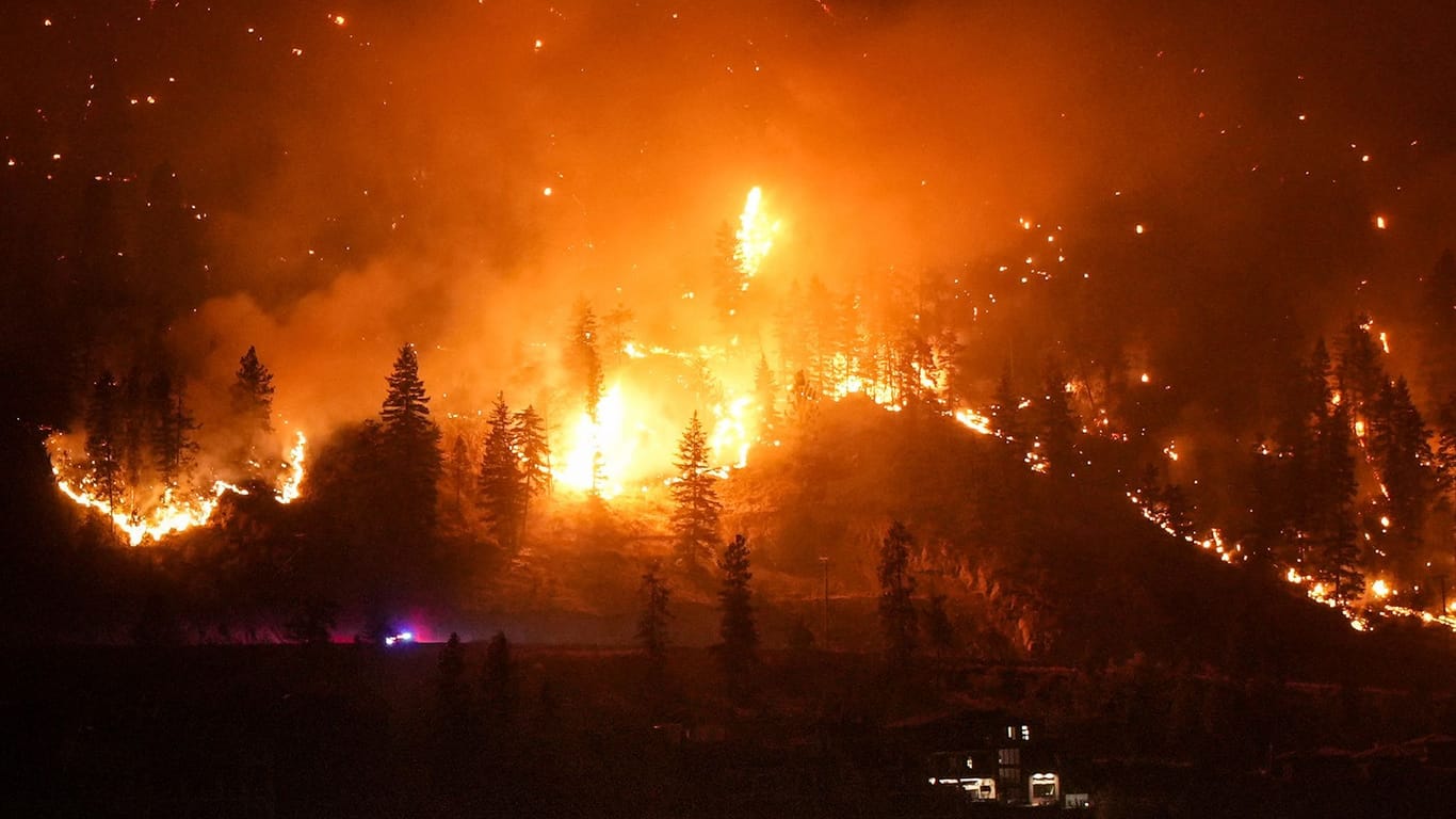 Ein Waldbrand am McDougall Creek an einem Berghang oberhalb eines Hauses am Seeufer.