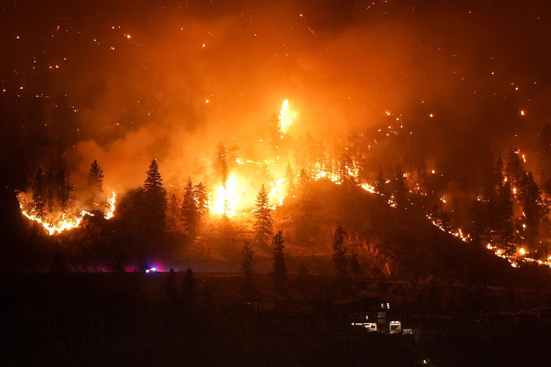 Ein Waldbrand am McDougall Creek an einem Berghang oberhalb eines Hauses am Seeufer.