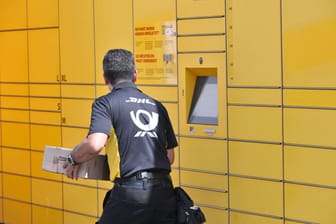 Ein Postbote der Deutschen Post füllt Pakete einer Packstation auf (Symbolbild). In Berlin ist ein Postbote dabei verletzt worden.