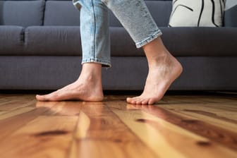 Füße einer Frau, die barfuß auf Holzboden geht