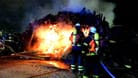 Feuerwehrleute löschen den hohen Holzhaufen nahe einer Bahnstrecke: Erneut sorgt ein Feuer entlang von Bahntrassen bei Hamburg für Aufsehen.