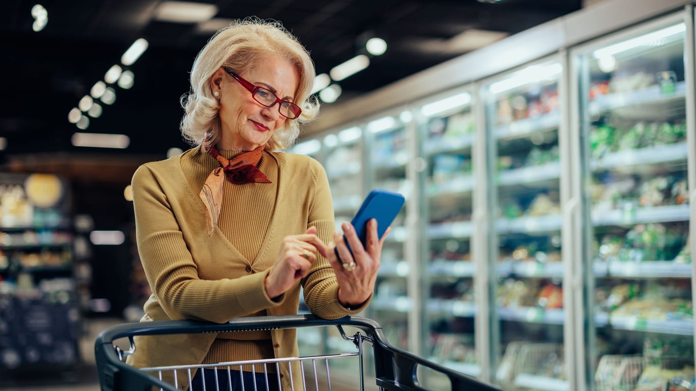 Frau im Supermarkt schaut auf ihr Handy