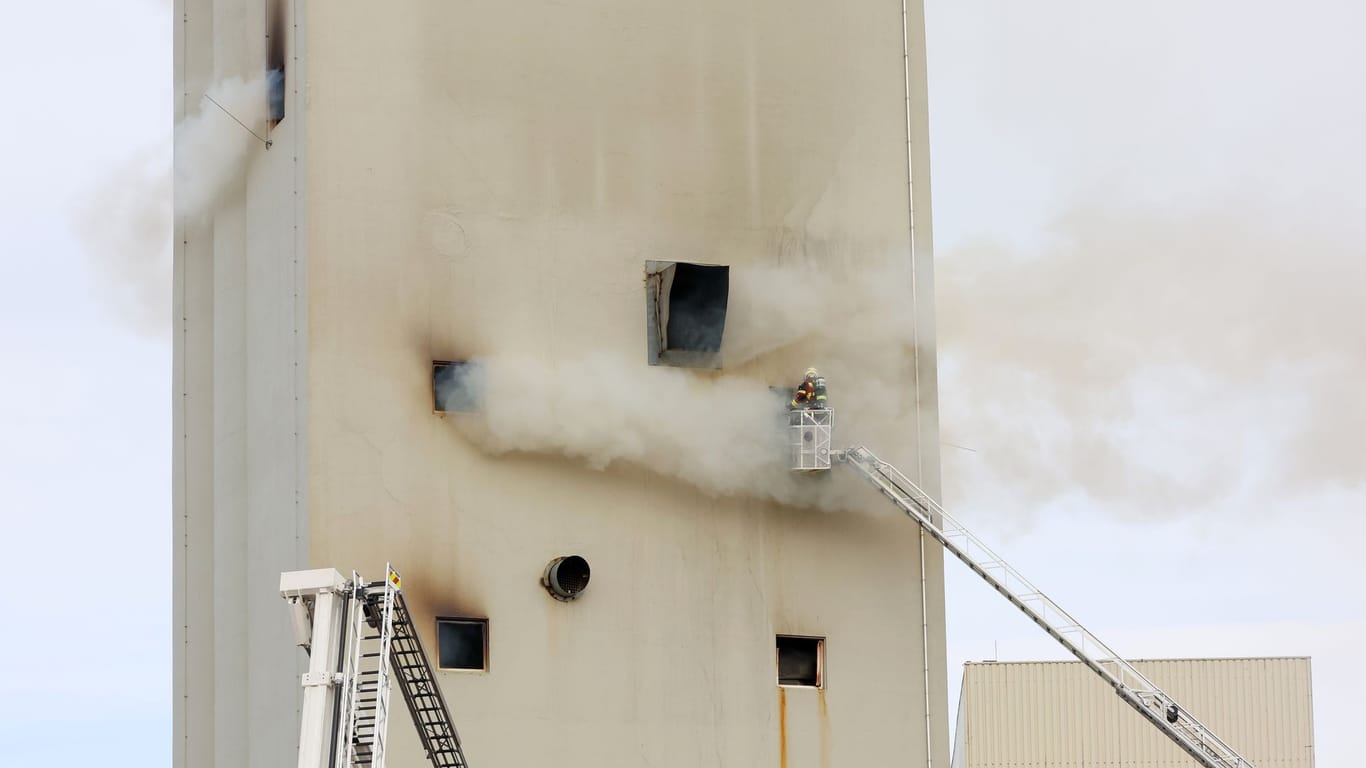 Ein Silo im Kreis Ditmarschen in Brand: Ein Feuerwehrmann steht auf einer Drehleiter an der Brandstelle.