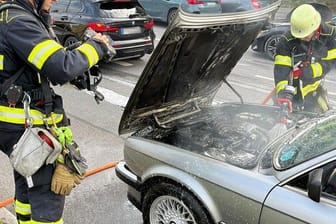 Einsatzkräfte der Feuerwehr München löschen den in Brand geratenen BMW.