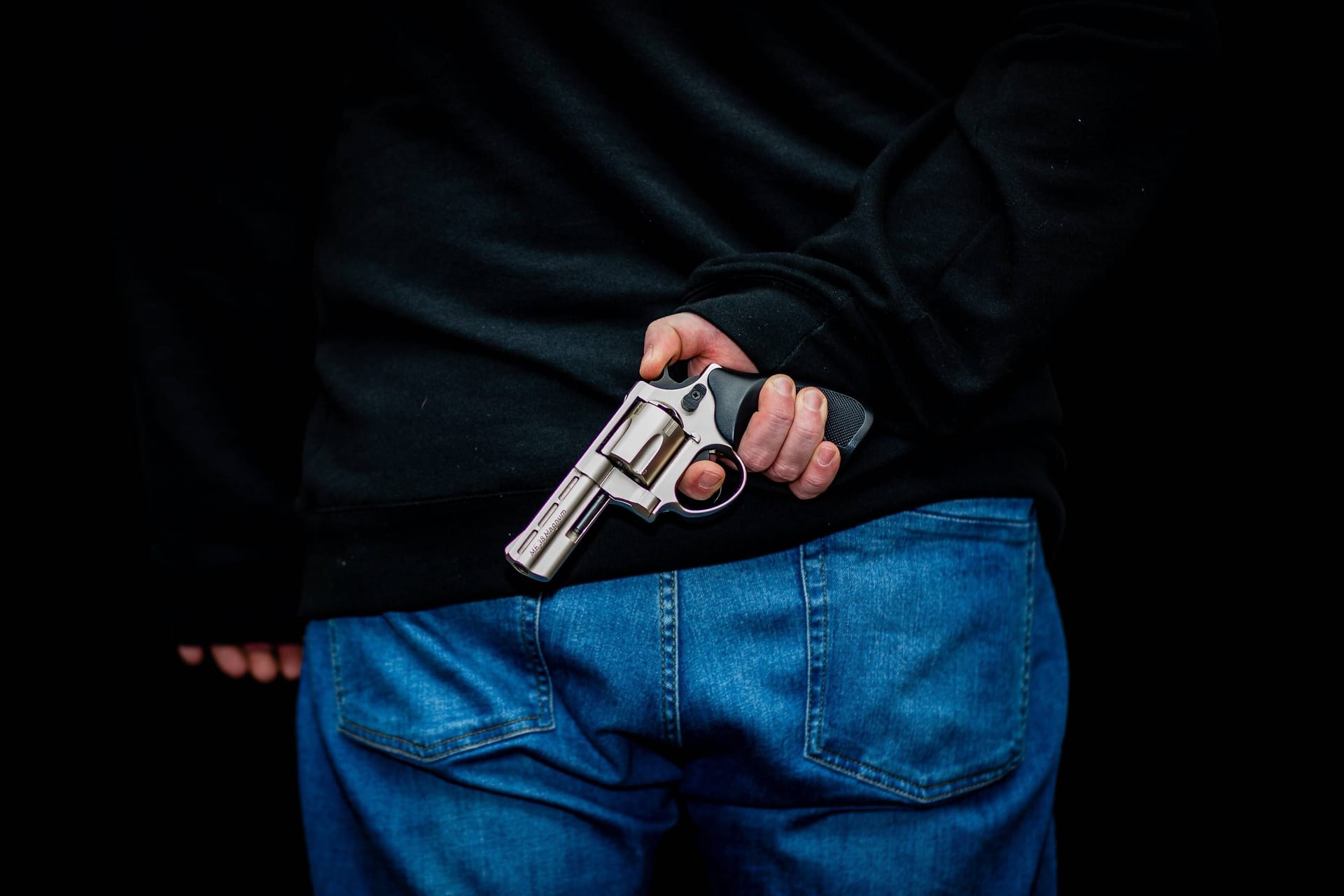 Ein Mann hält eine Waffe hinter dem Rücken (Symbolbild): Der Täter überfiel eine Tankstelle mit einem Schreckschussrevolver.