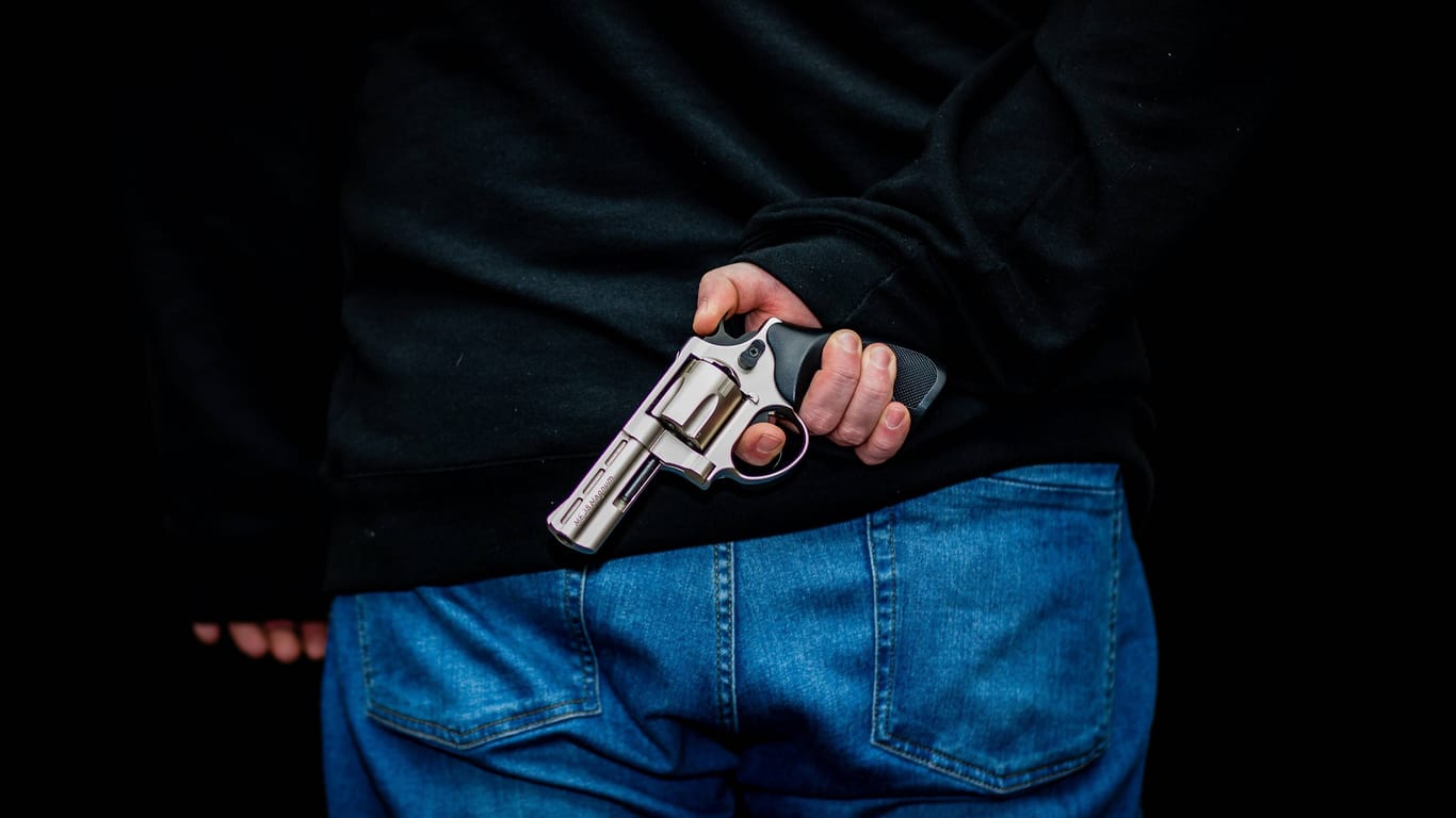 Ein Mann hält eine Waffe hinter dem Rücken (Symbolbild): Der Täter überfiel eine Tankstelle mit einem Schreckschussrevolver.