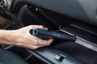 Ein Mann hält in seinem Auto eine Pistole in der Hand (Symbolbild): Im Handschuhfach des Wagens fand die Polizei eine Schreckschusswaffe.