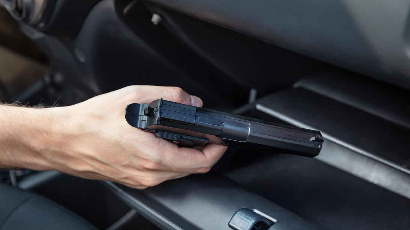 Ein Mann hält in seinem Auto eine Pistole in der Hand (Symbolbild): Im Handschuhfach des Wagens fand die Polizei eine Schreckschusswaffe.