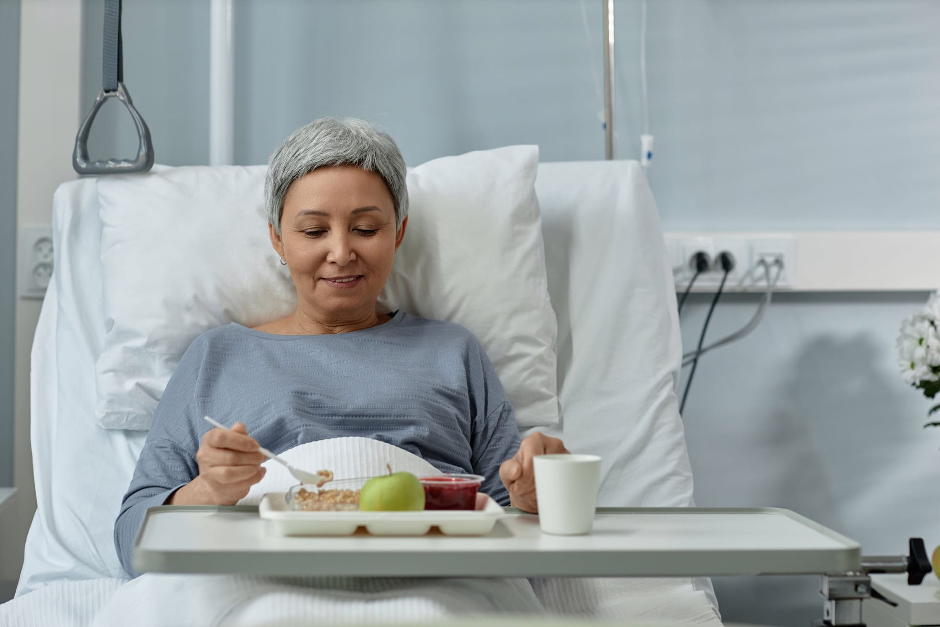 Eine Frau sitzt im Krankenhausbett und nimmt eine Mahlzeit zu sich.