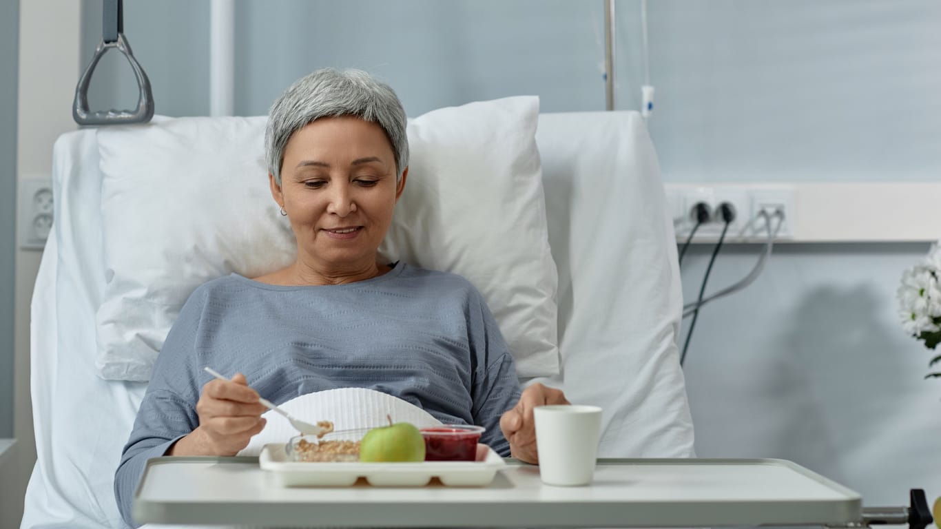 Eine Frau sitzt im Krankenhausbett und nimmt eine Mahlzeit zu sich.