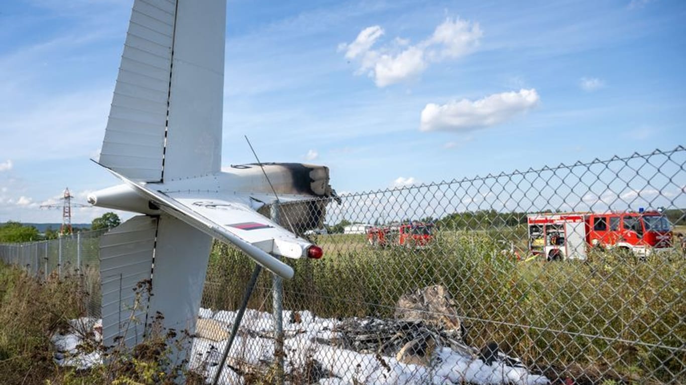 Trümmerteile eines Flugzeugs hängen in einem Zaun, während Fahrzeuge der Feuerwehr am Einsatzort stehen.