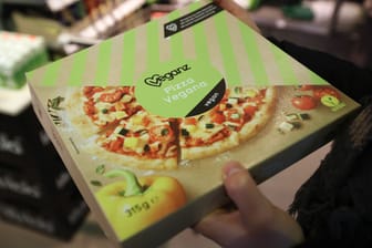 Ein Mann hält eine Tiefkühlpizza in der Hand (Symbolbild): Weil ihm sein Essen herunterfiel, kam ein Betrunkener in Freising ins Krankenhaus.