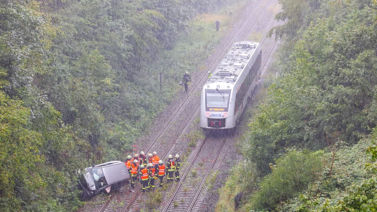 Der Wagen liegt seitlich auf der Bahnstrecke – knapp neben einer herannahenden S-Bahn.