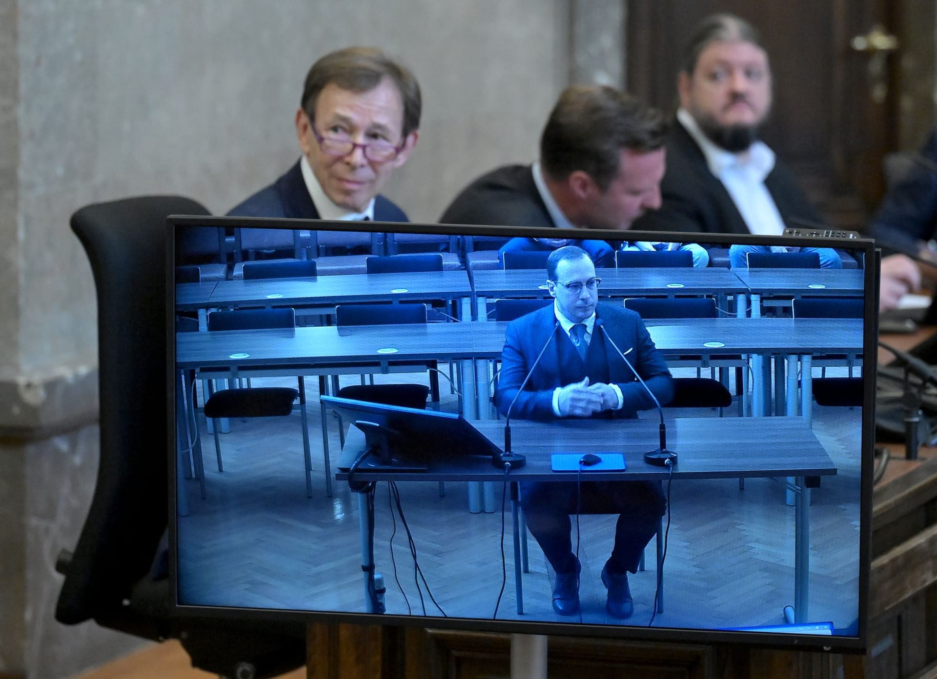 Wien: Der Angeklagte ehemalige Burgschauspieler Florian Teichtmeister auf einem Bildschirm sowie sein Anwalt Rudolf Mayer vor Verhandlungsbeginn.