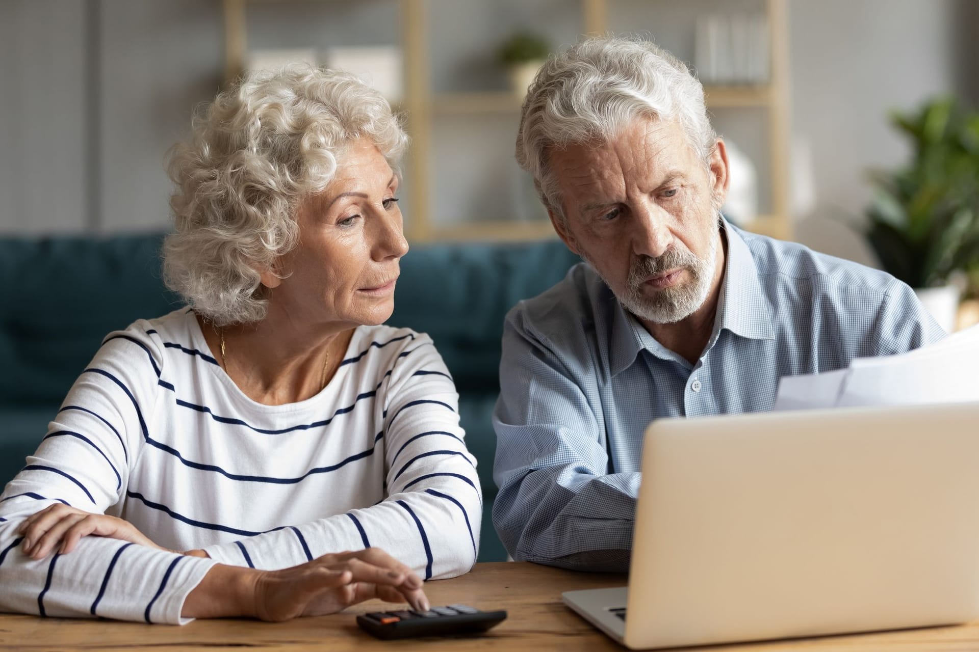 Focused middle aged retired family couple managing monthly budget, involved in financial paperwork, paying taxes online using e-banking computer application or calculating expenses together at home.