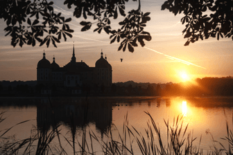 Die Sonne geht am Morgen hinter dem Schloss Moritzburg auf: So nutzen Sie den Spätsommer für Wochenendausflüge am besten.