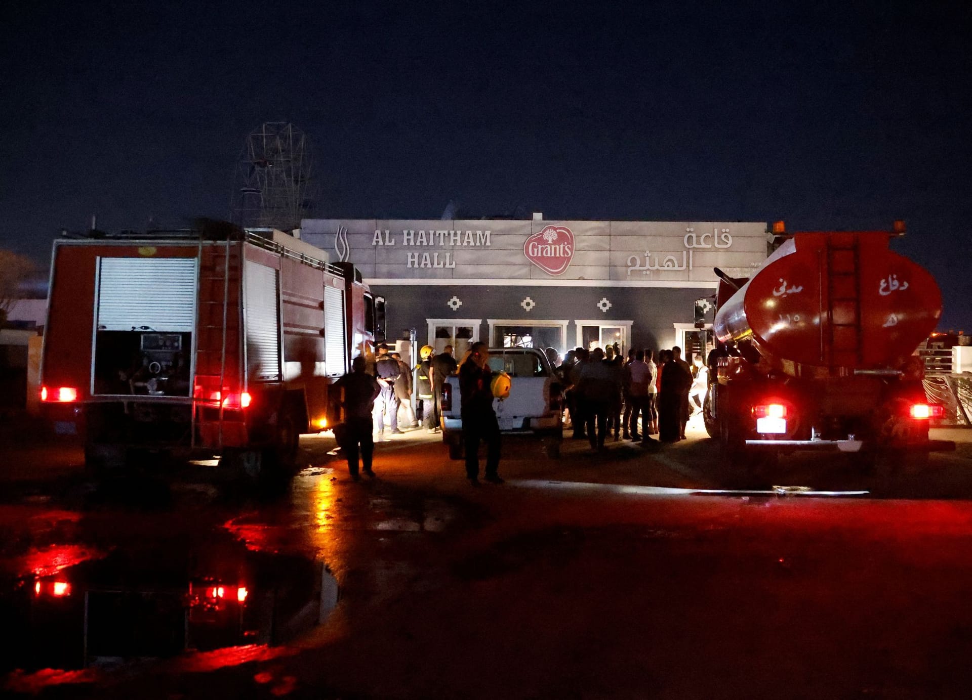 Rettungskräfte und Menschen vor der ausgebrannten Halle im Ort Al-Hamdanija.