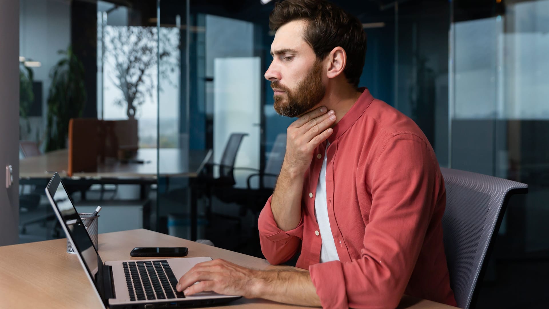 Mann am Laptop fasst sich an den Hals: Wer einen Kloß im Hals wegbekommen will, kann das auch mit Hausmitteln versuchen.