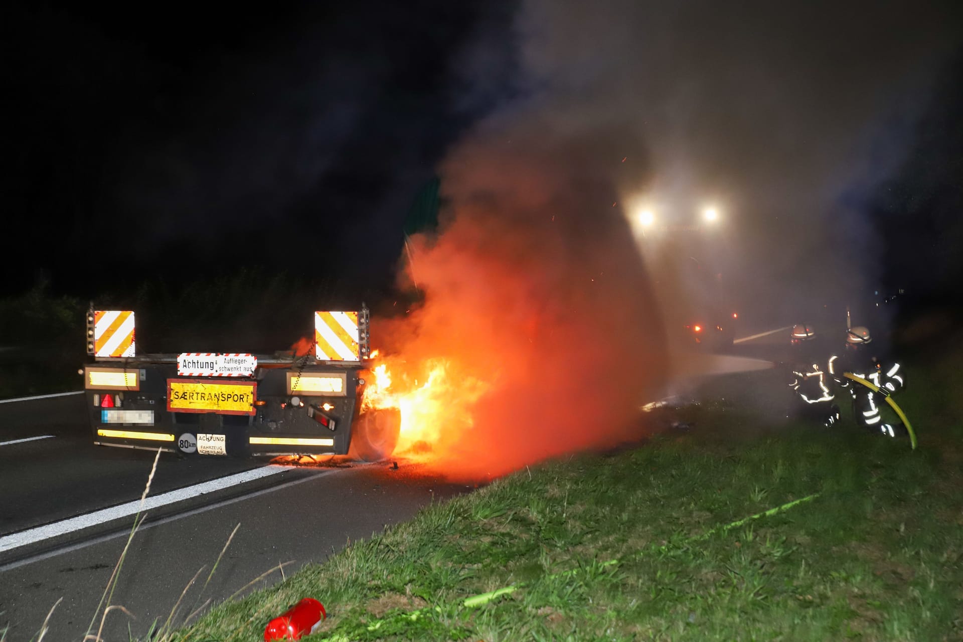 Feuerwehrleute löschen den brennenden Schwertransporter: Die Bergung des Lkws gestaltet sich schwierig.