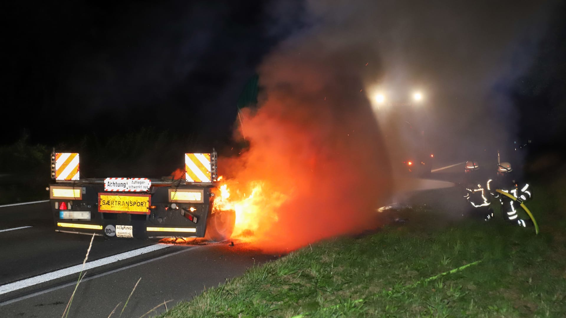 Feuerwehrleute löschen den brennenden Schwertransporter: Die Bergung des Lkws gestaltet sich schwierig.