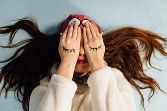 Frau mit Schlafmaske bedeckt die Augen mit den Händen: Wie viel wissen Sie über Schlaf? Testen Sie sich.