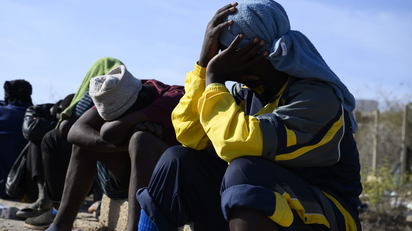Migranten sitzen bei großer Hitze in einer Notunterkunft auf der italienischen Mittelmeerinsel Lampedusa.