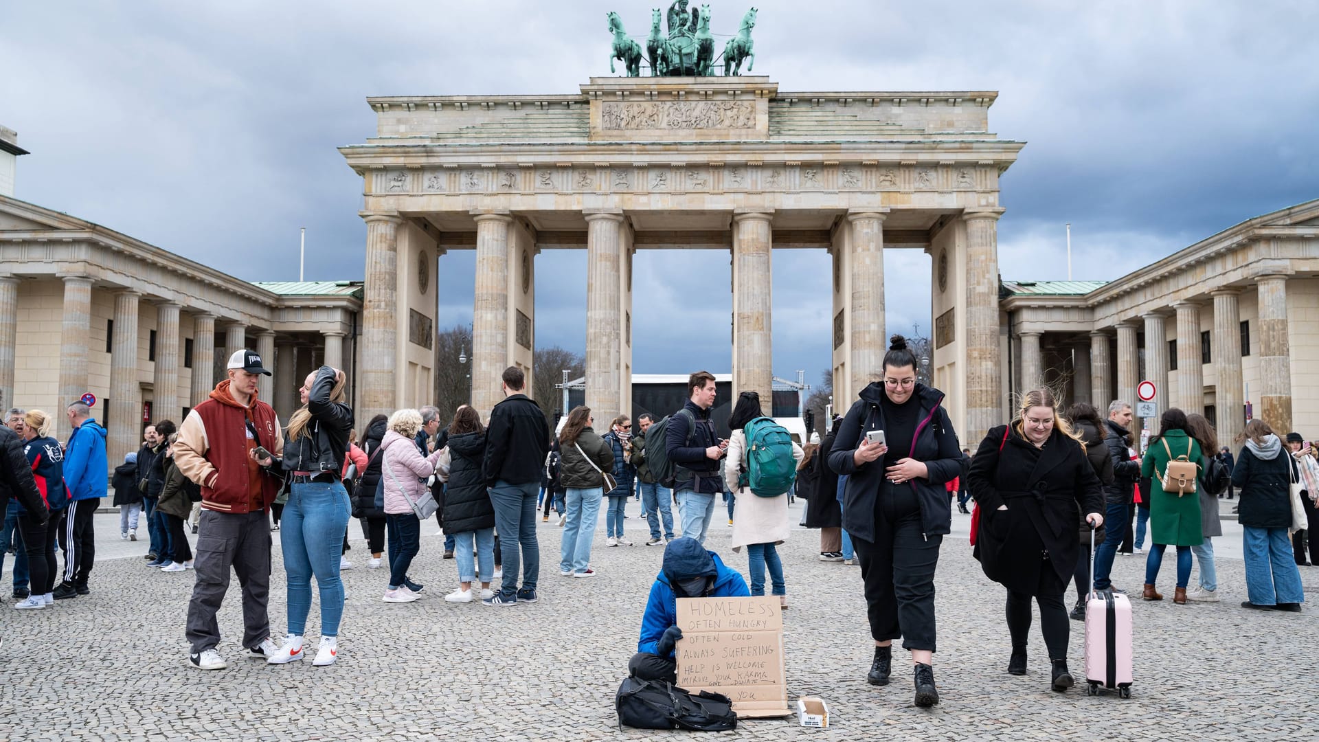 Ein Wohnungsloser bettelt mit einem Schild auf dem Pariser Platz vor dem Brandenburger Tor.