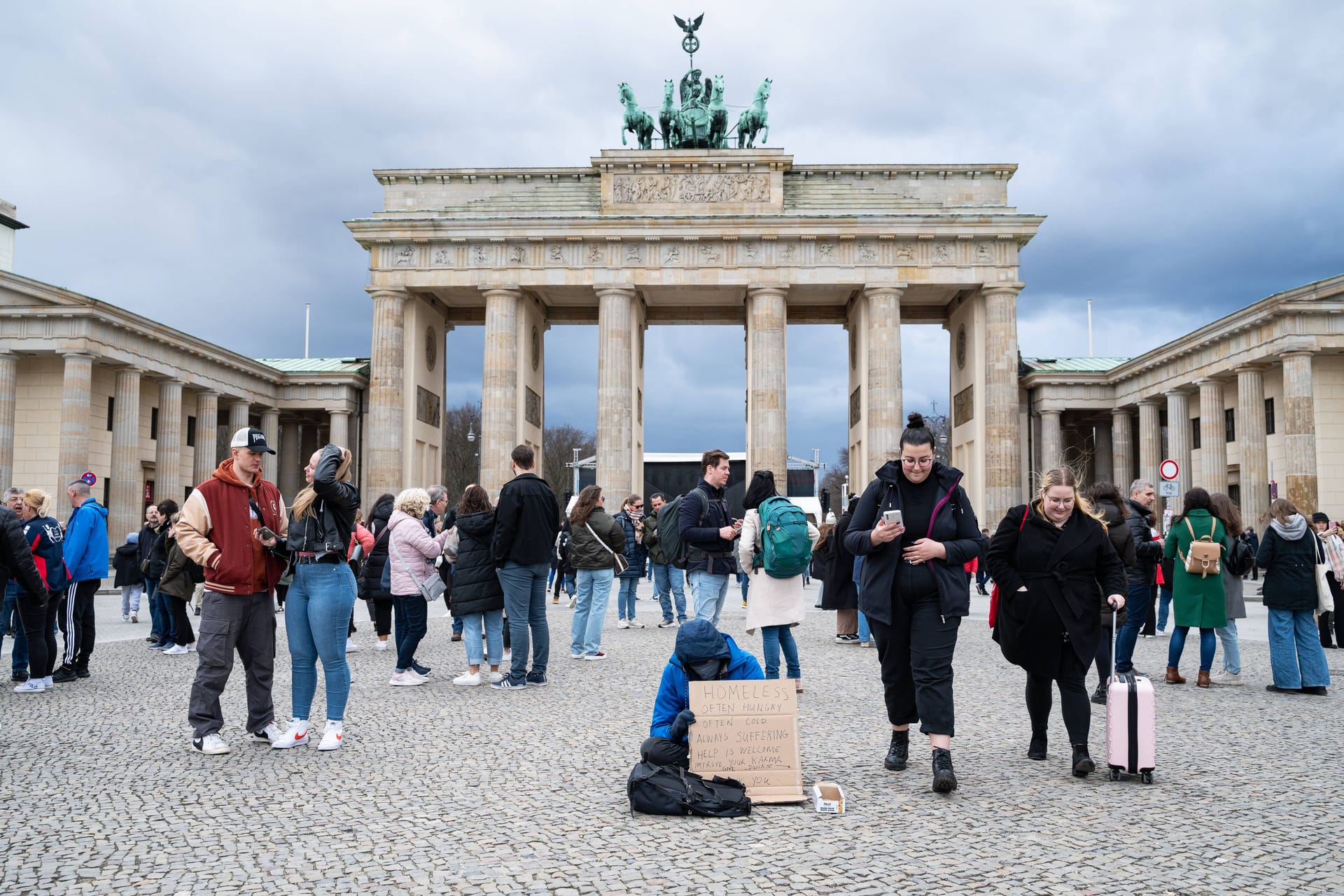 Ein Wohnungsloser bettelt mit einem Schild auf dem Pariser Platz vor dem Brandenburger Tor.