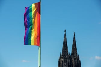 Regenbogenfahne mit Kölner Dom vor blauem Himmel: In Köln findet am Mittwoch ein Segnungsgottesdienst statt.