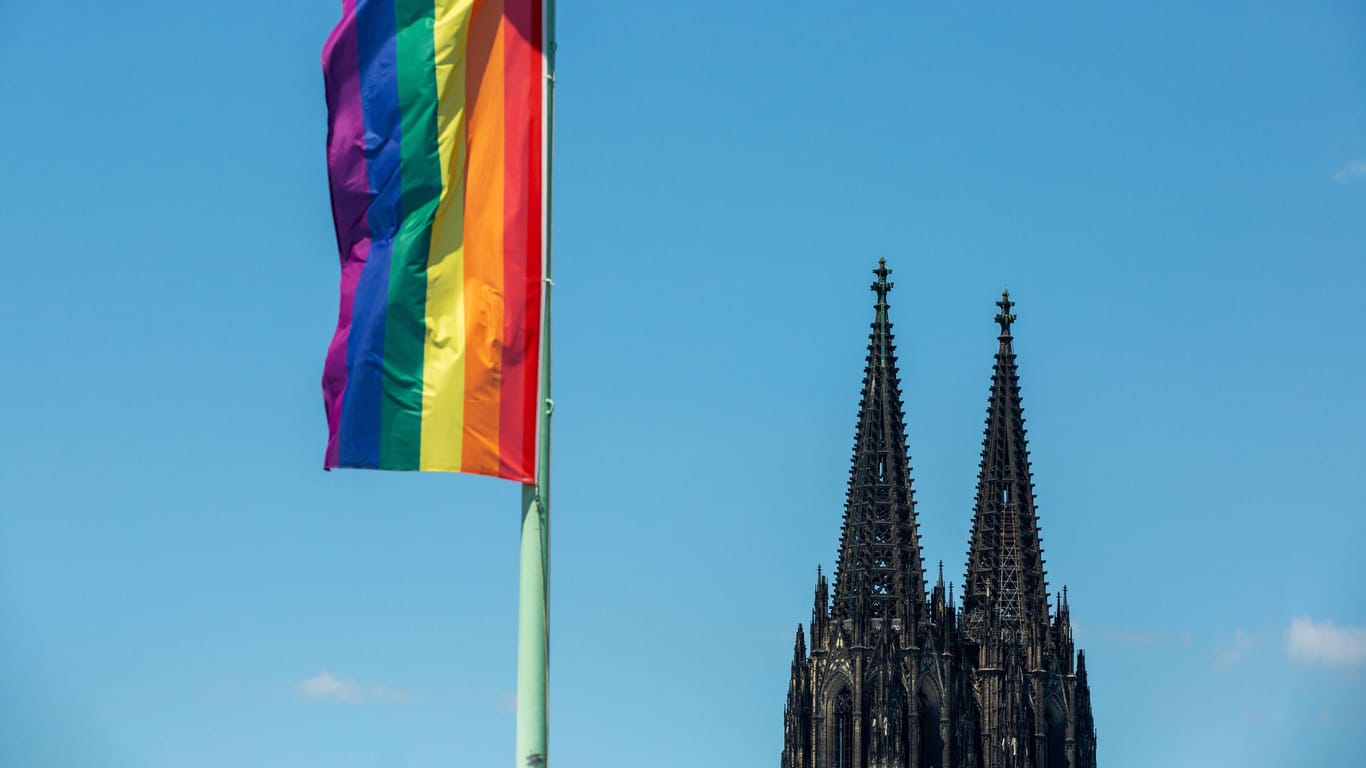 Regenbogenfahne mit Kölner Dom vor blauem Himmel: In Köln findet am Mittwoch ein Segnungsgottesdienst statt.